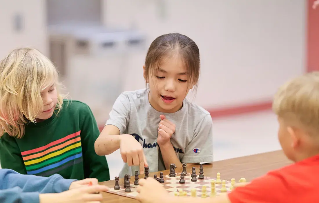 Three children are engaged in playing a game of chess at a table.