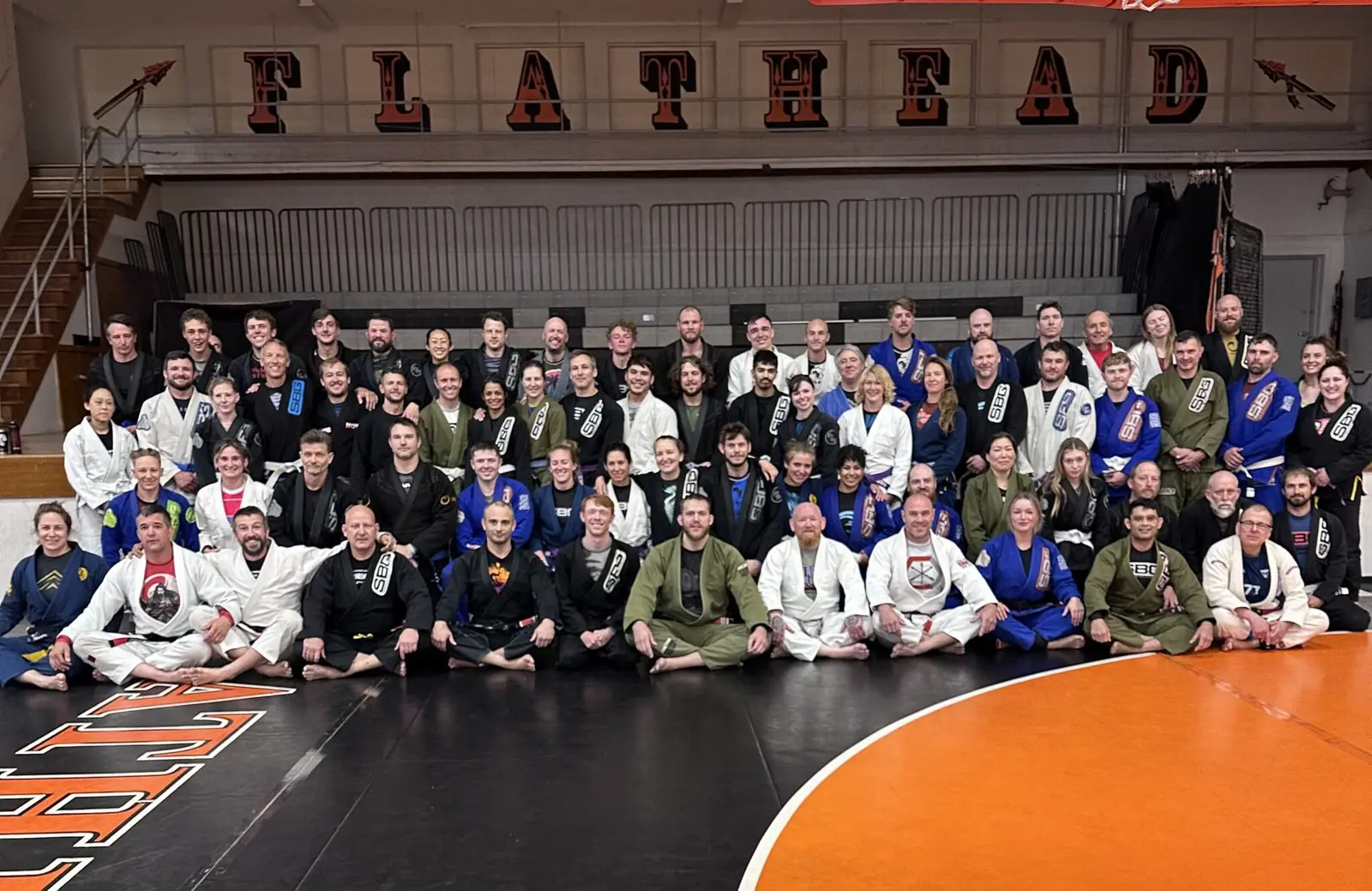 A large group of people wearing martial arts uniforms gather for a photo on a gymnasium mat.