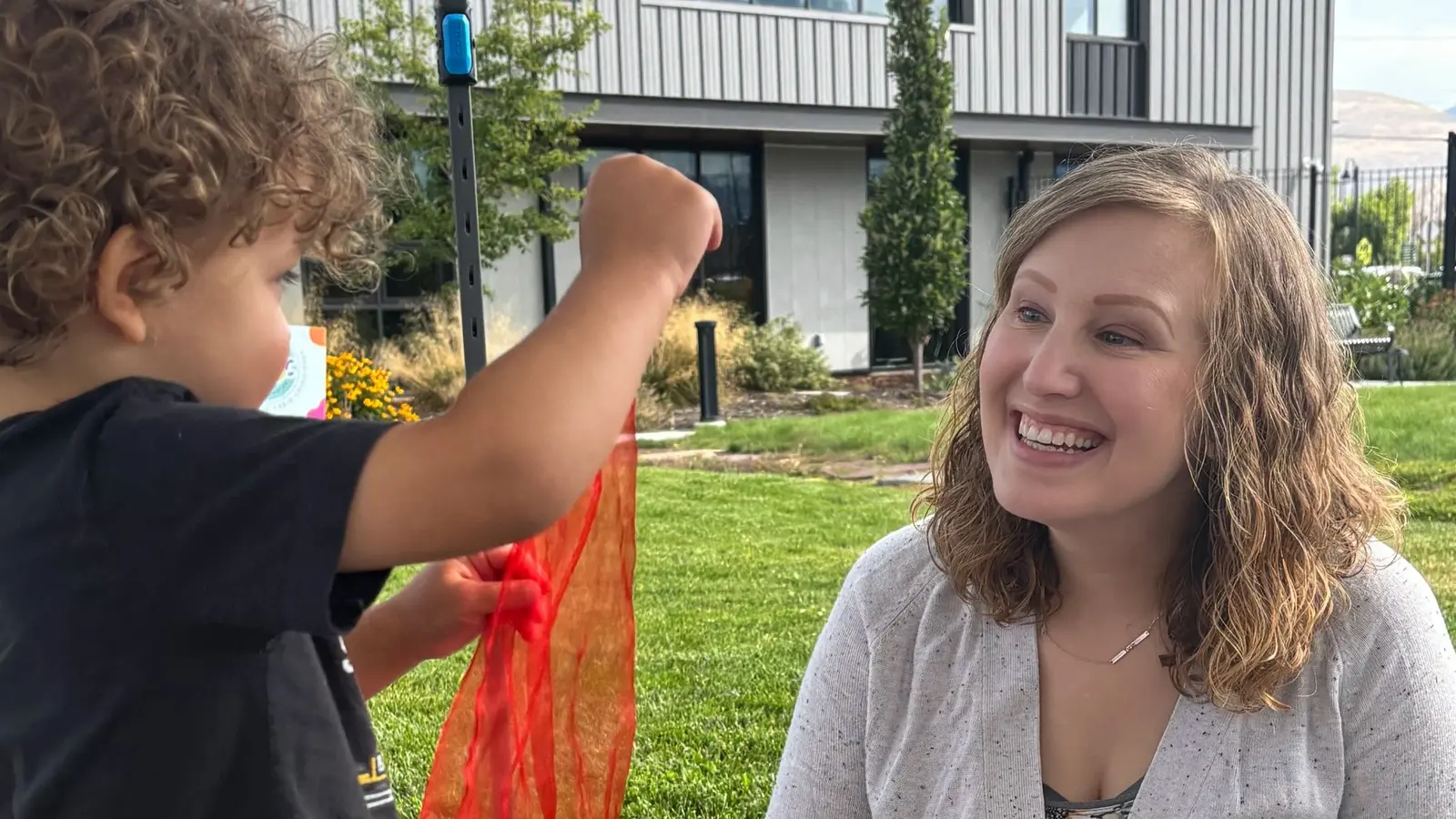A woman smiles while interacting with a young child who is holding a red scarf.