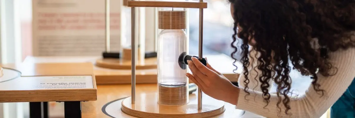 person playing with a magnet and iron filings inside a glass cylindar