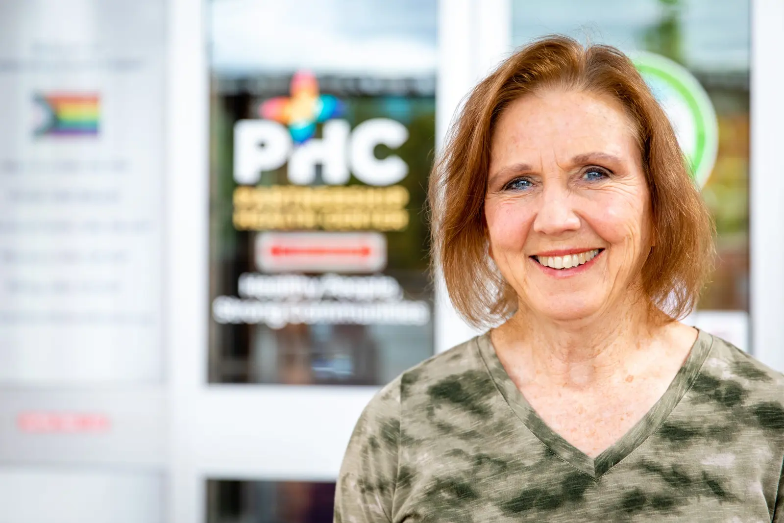 A smiling woman stands in front of a glass door with signage.