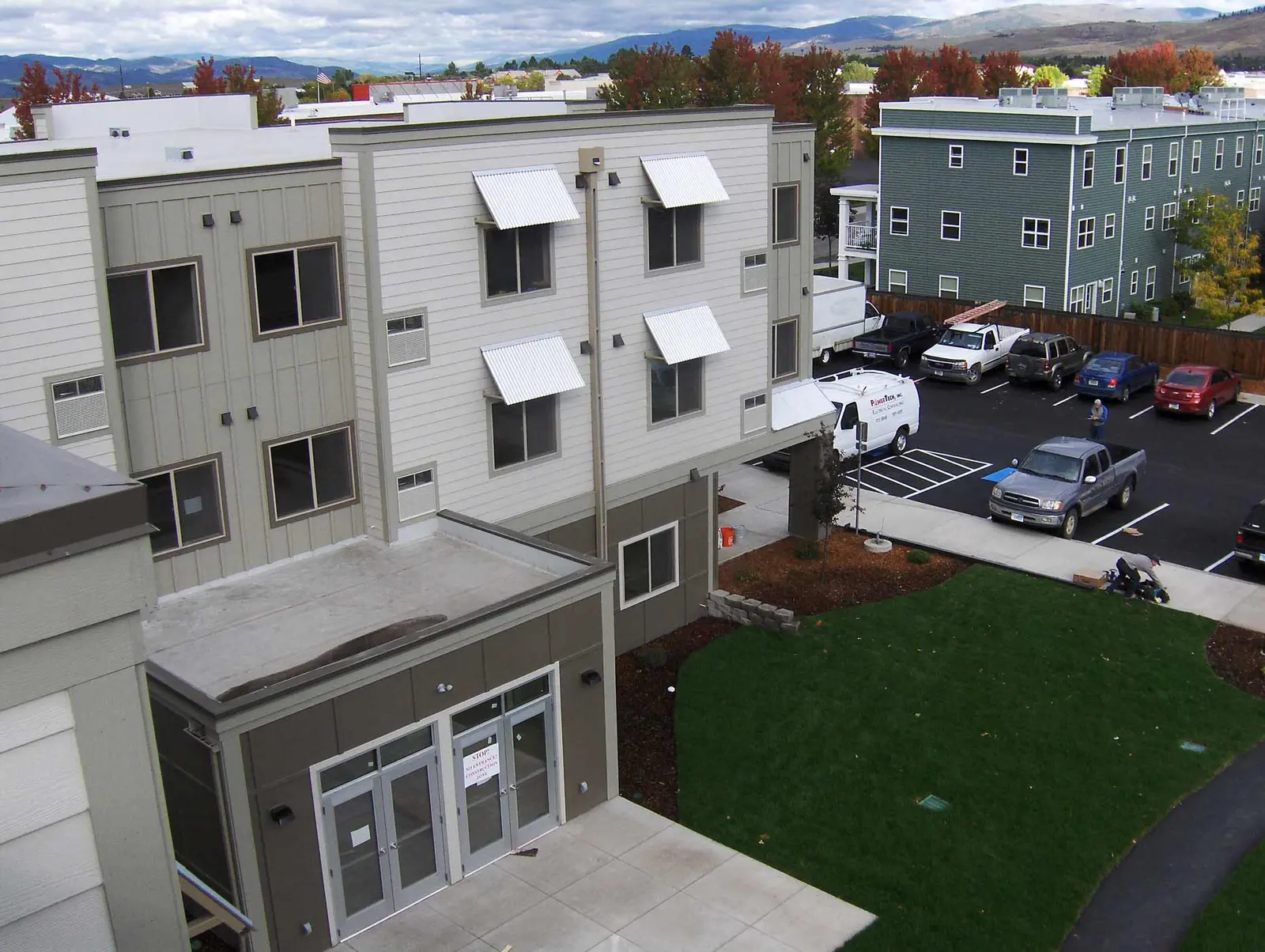 An aerial view of a multi-story apartment building with a parking lot and lawn.