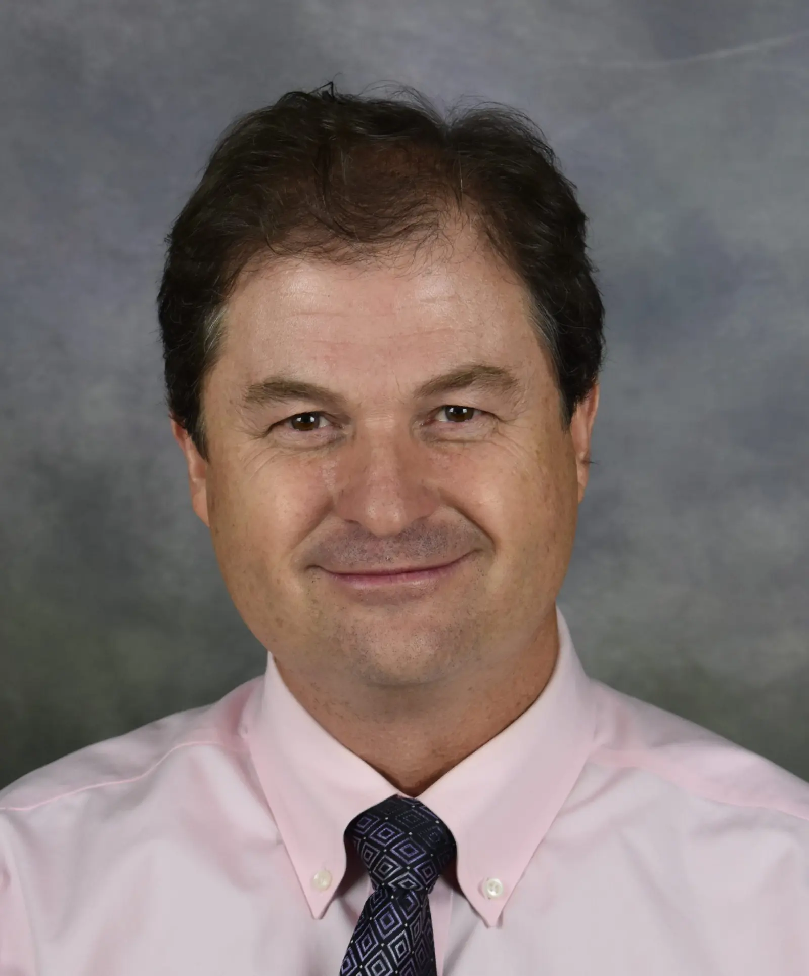 A headshot portrait of an adult man against a gray backdrop.