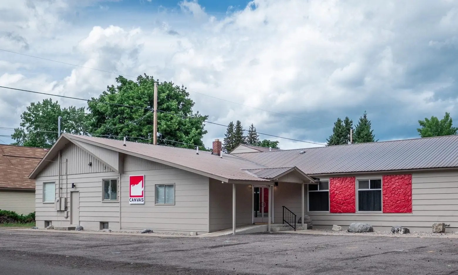The exterior of a commercial building featuring light gray siding and red decorative panels.