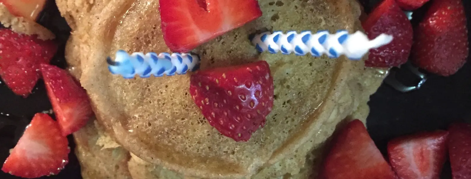 A stack of pancakes decorated with strawberries and birthday candles.