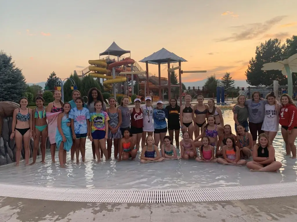 A group of young people pose for a photo in a shallow pool at a water park at sunset.