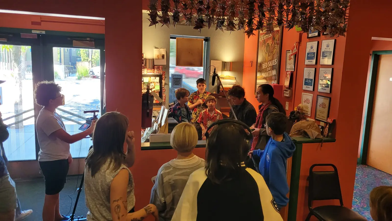 A group of young people and an adult are filming a scene inside a room decorated with origami cranes.
