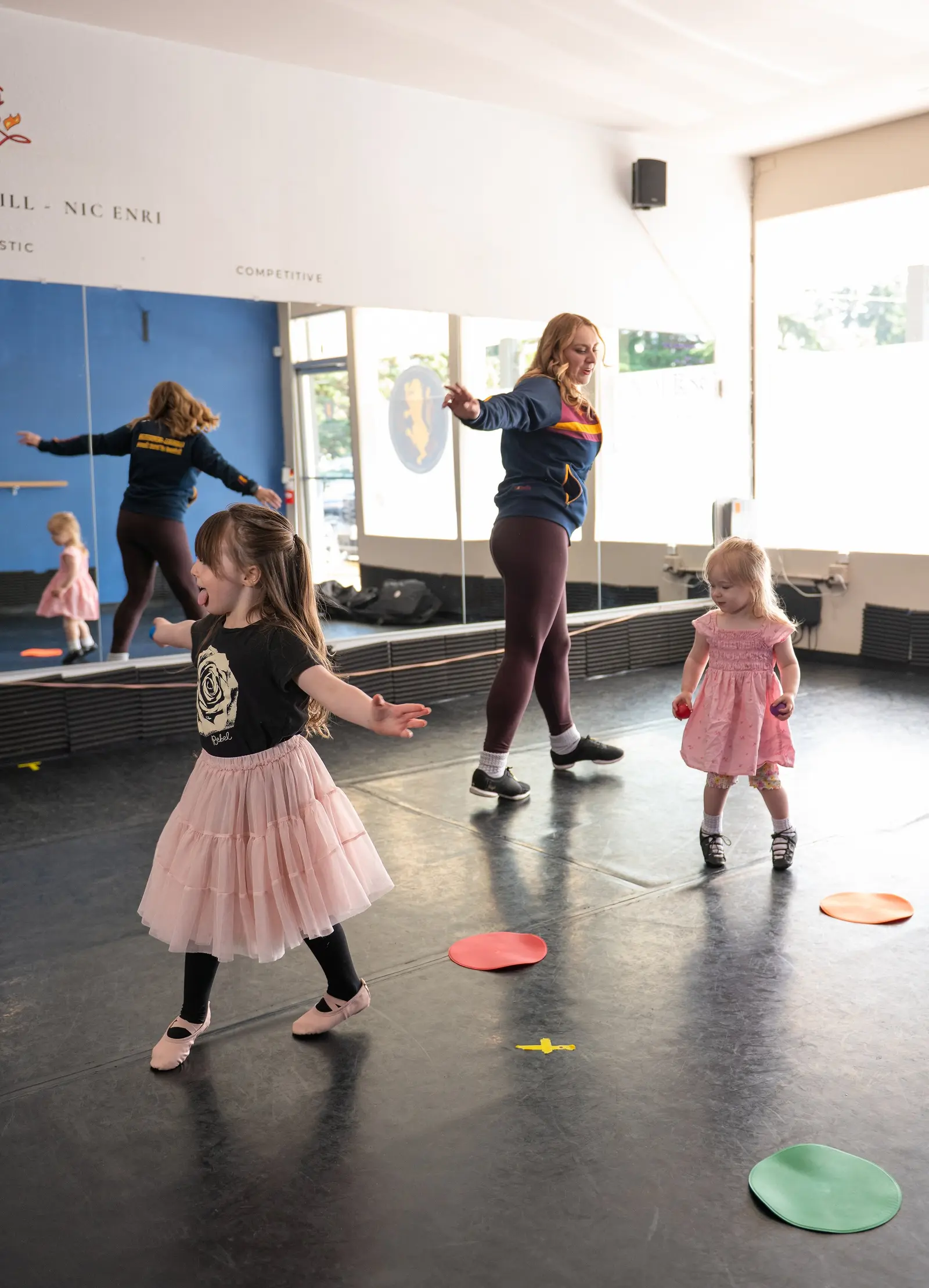 An instructor leads two young children in a dance activity in a studio.