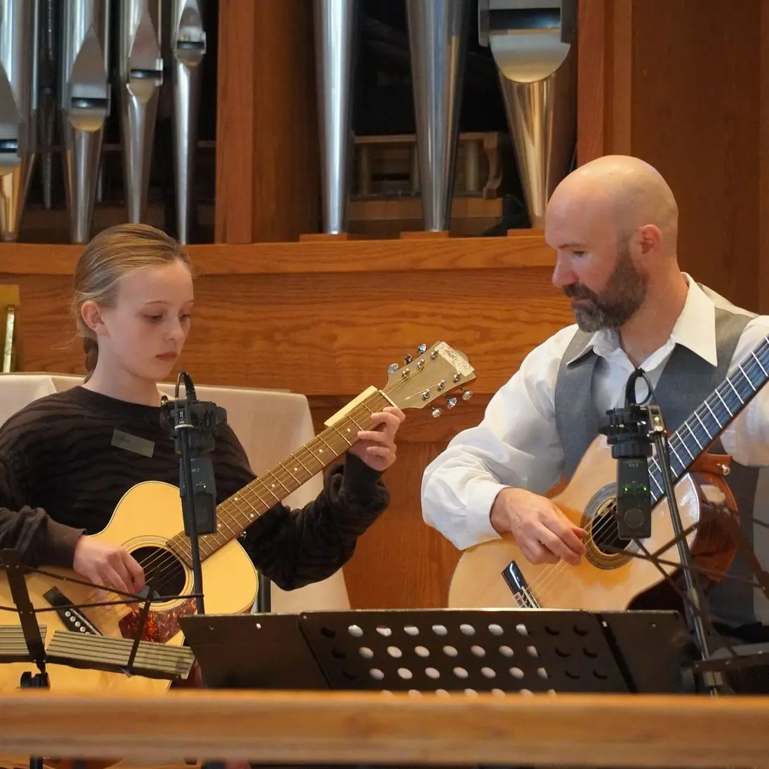 Two people playing guitars together indoors.