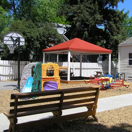 A backyard playground area features a wooden bench, a basketball hoop, a playhouse, and a small gazebo.