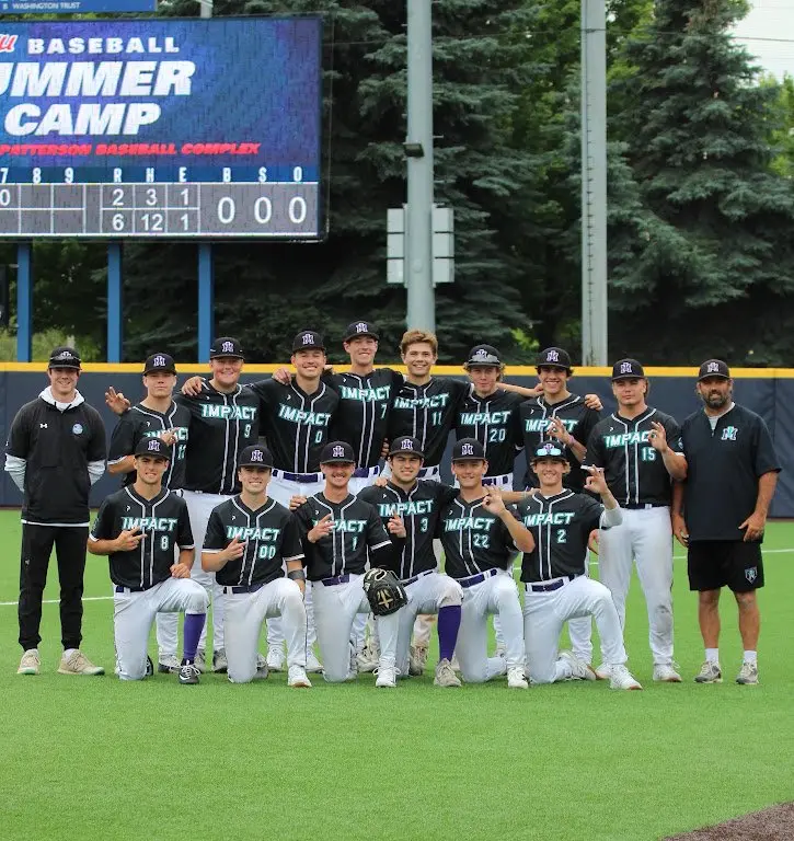 A baseball team poses for a group photo on a field in front of a scoreboard.