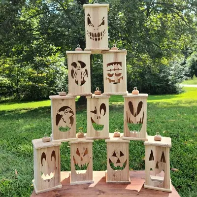 A pyramid stack of wooden lanterns with various carved Halloween-themed faces stands on a wooden surface outdoors.