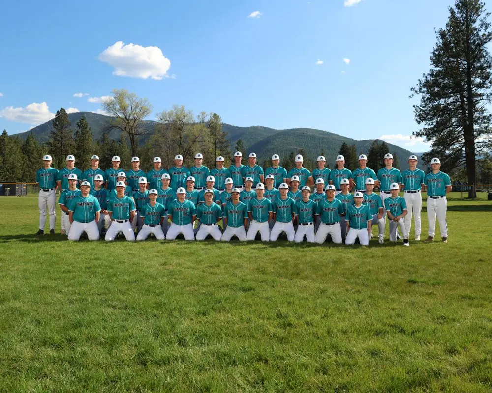 A baseball team in matching teal uniforms poses for a group photograph on a field.