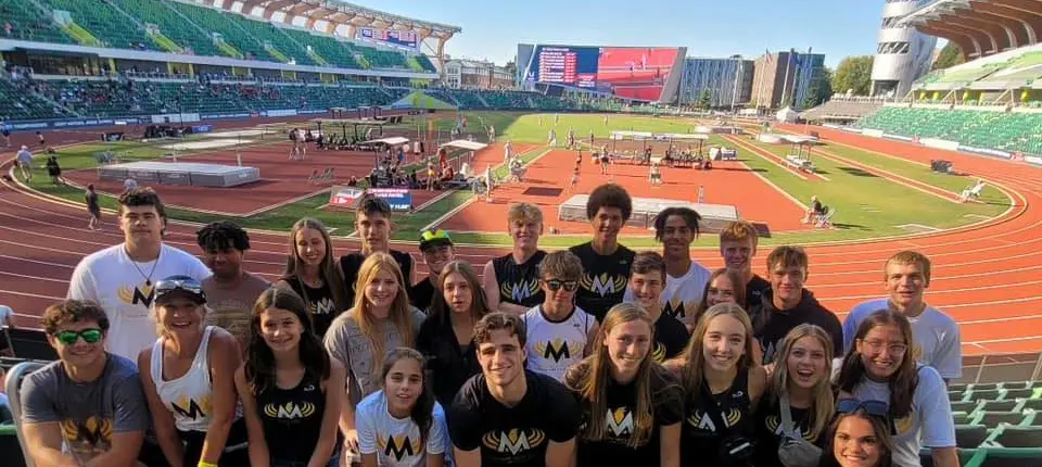 A large group of people wearing matching shirts poses for a photo at a stadium track.