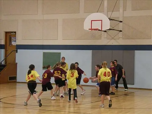 A group of young basketball players practices on an indoor court with their instructor.
