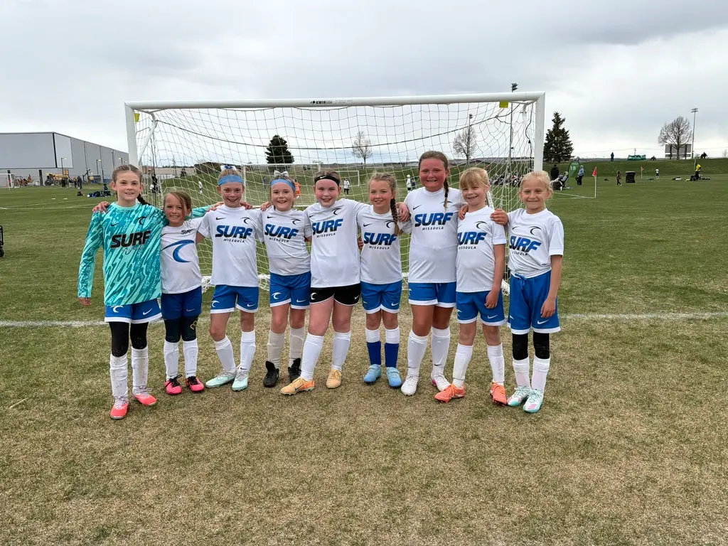 A youth girls soccer team stands together for a photo in front of a soccer goal.