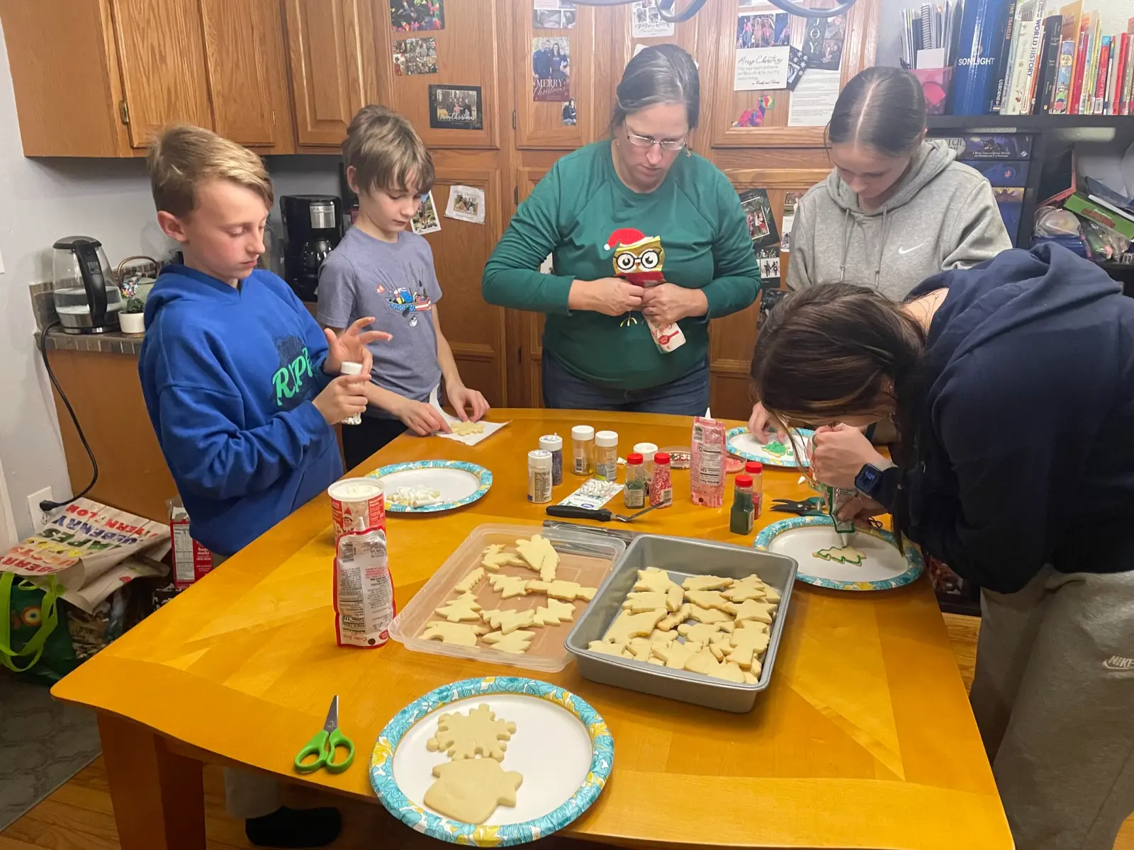 A family gathers around a kitchen table to decorate holiday sugar cookies together.
