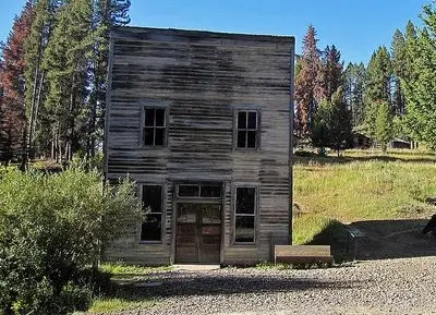 A rustic two-story wooden building stands in a clearing surrounded by trees.
