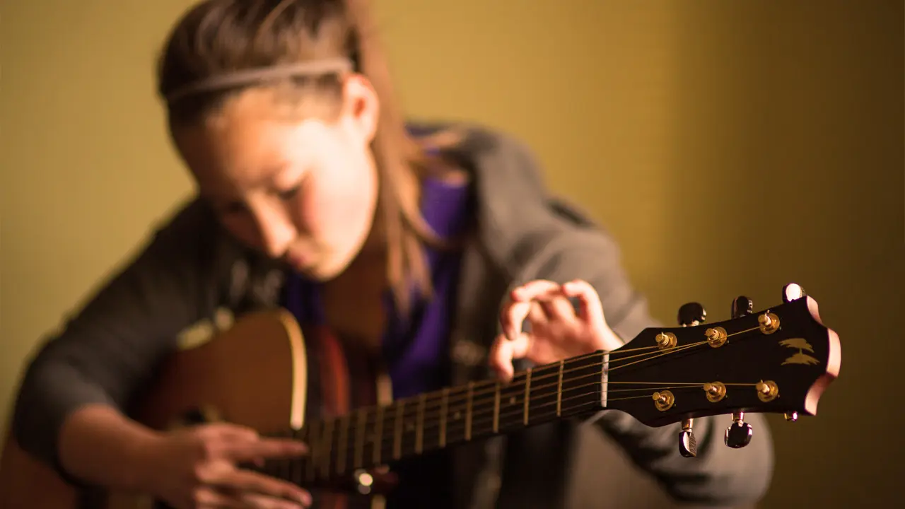 A young girl is focused on playing an acoustic guitar.