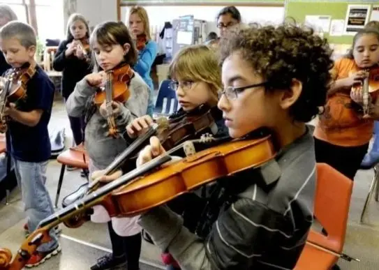 A group of children plays violins during a music class.