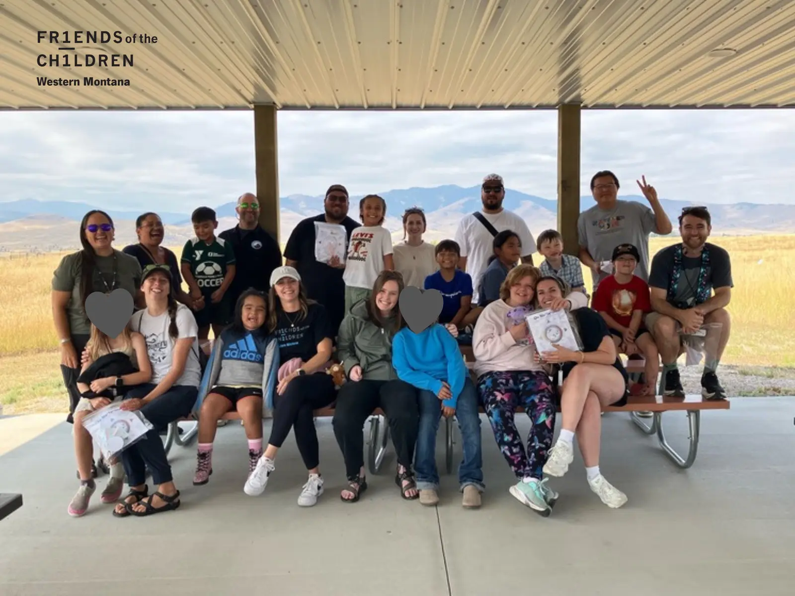 A group of adults and children pose for a photograph together at an outdoor pavilion.