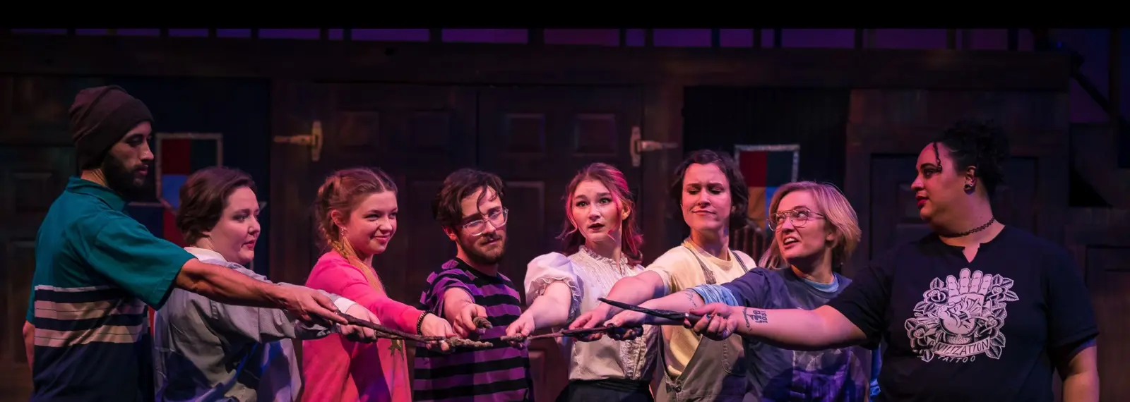 A group of young adults stand in a line on a stage, holding out their hands together.