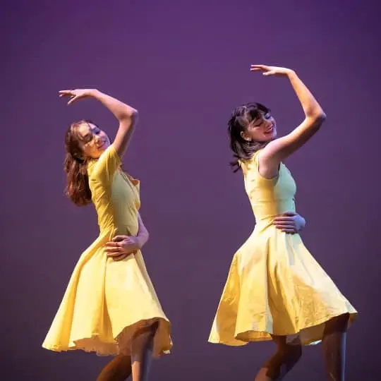 Two performers in yellow dresses pose on stage.