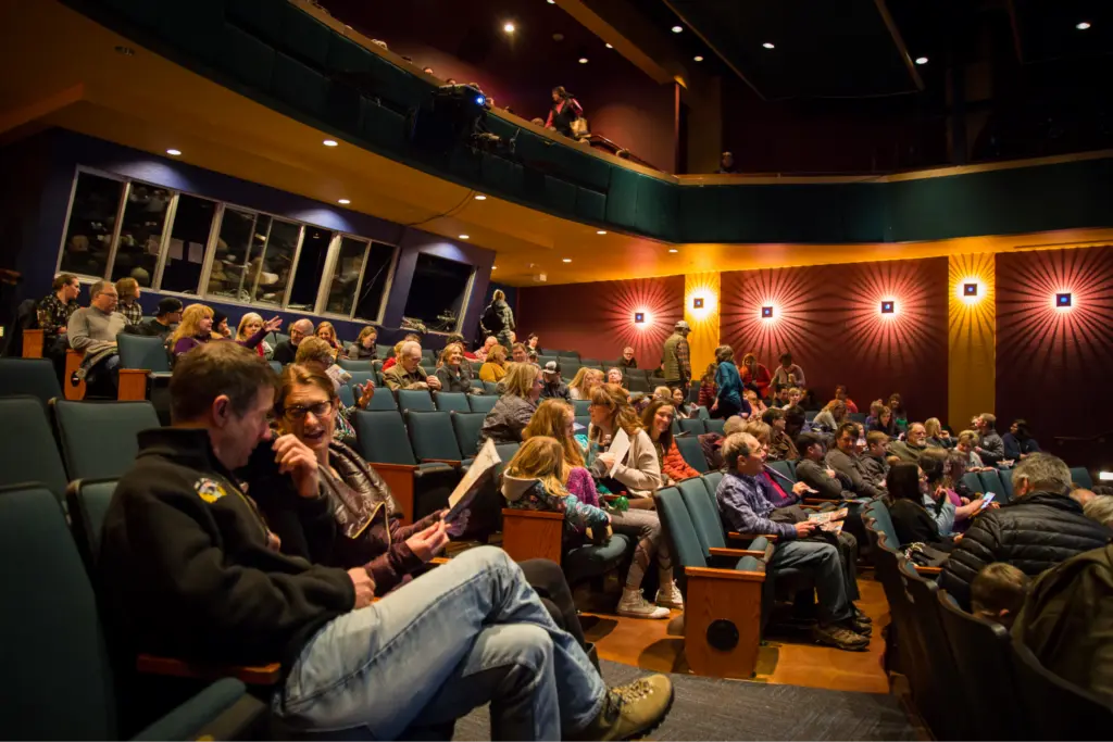 An audience sits in an indoor theater venue waiting for an event to begin.