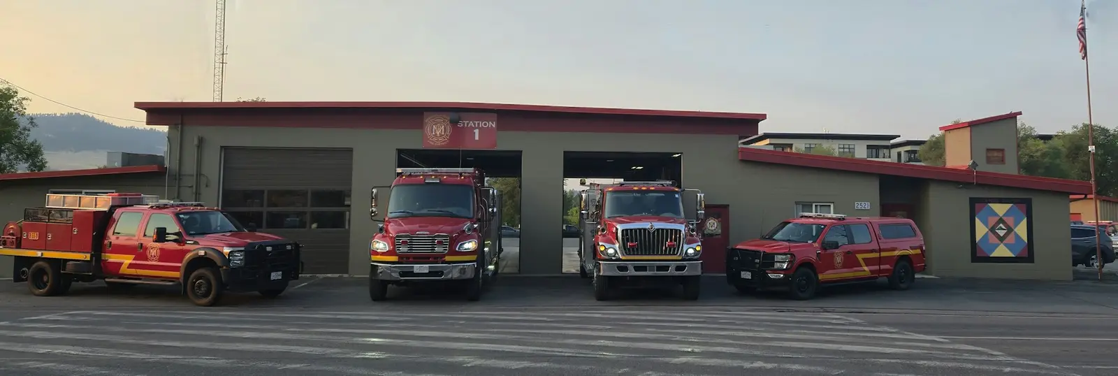 A fire station labeled "STATION 1" featuring several fire trucks and emergency vehicles parked outside.