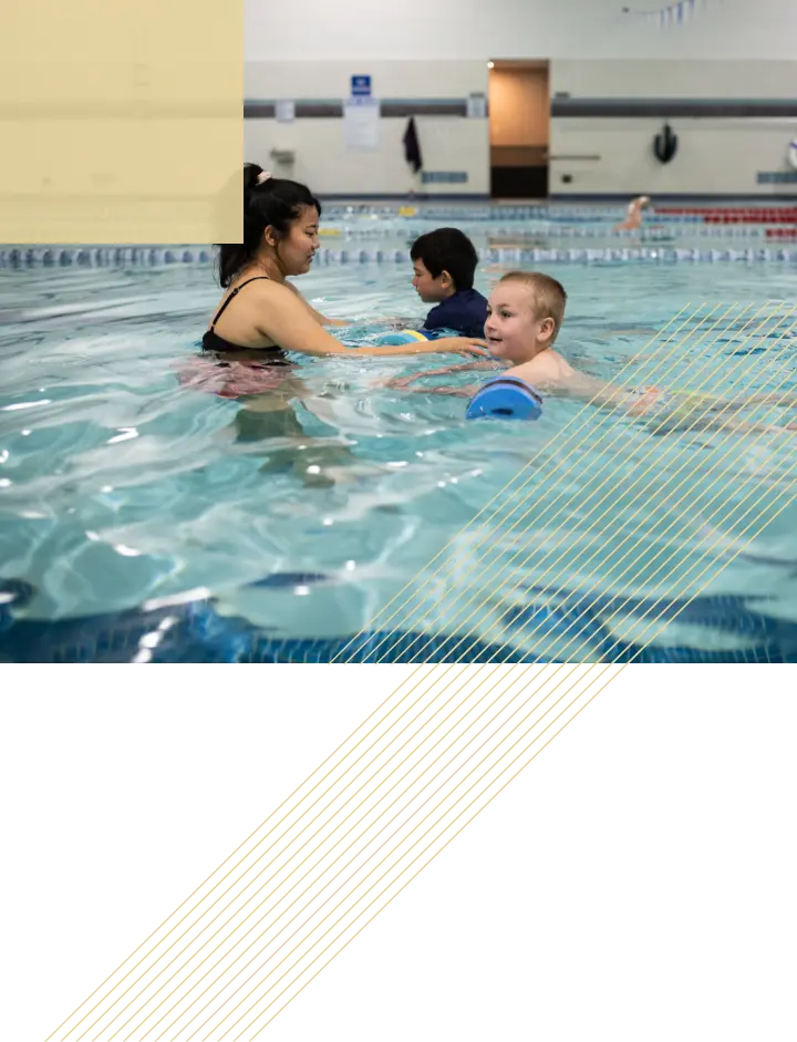 A swimming instructor teaches two young children to swim in an indoor pool.