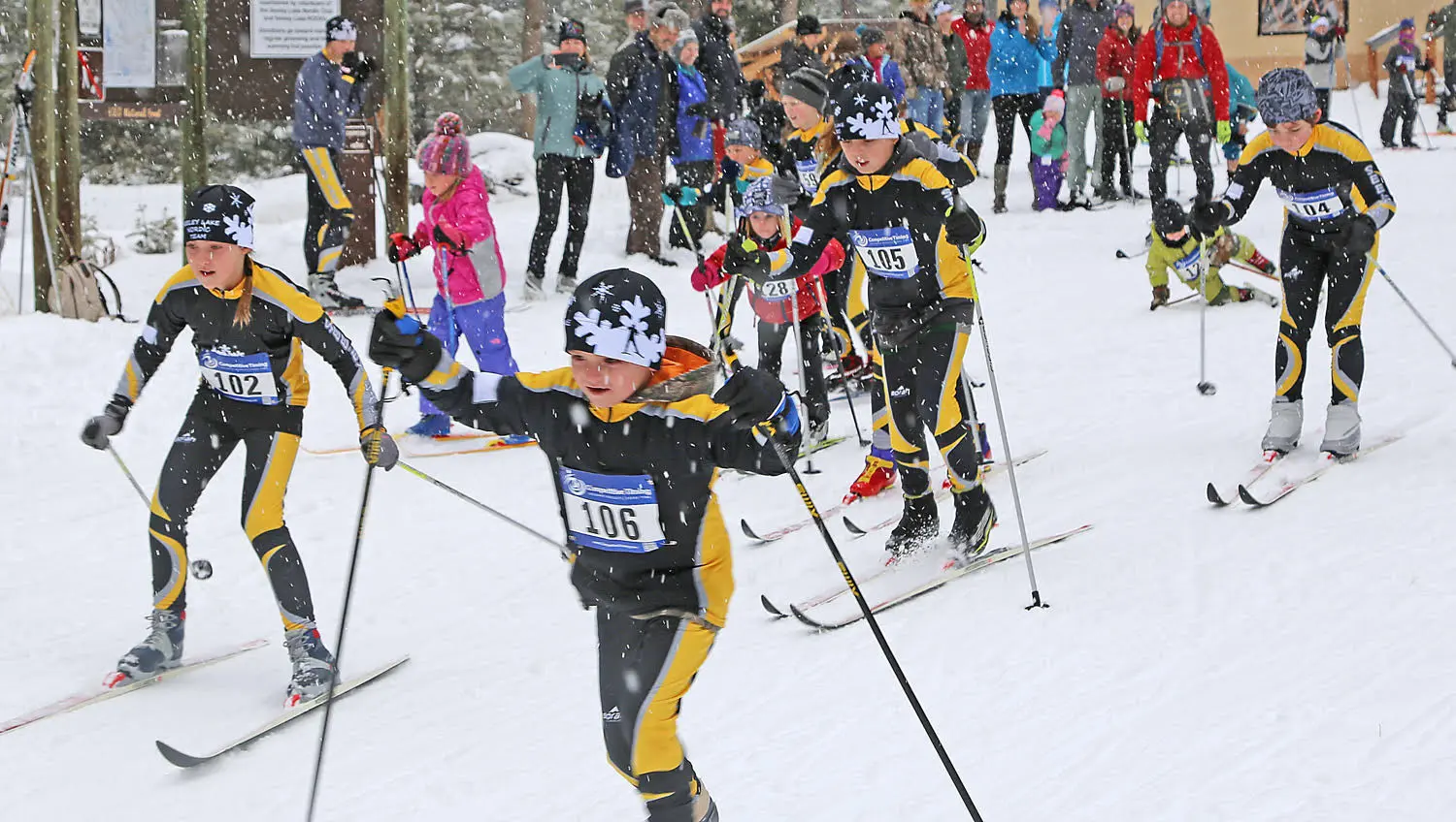 A group of children compete in a cross-country ski race during a snowfall.