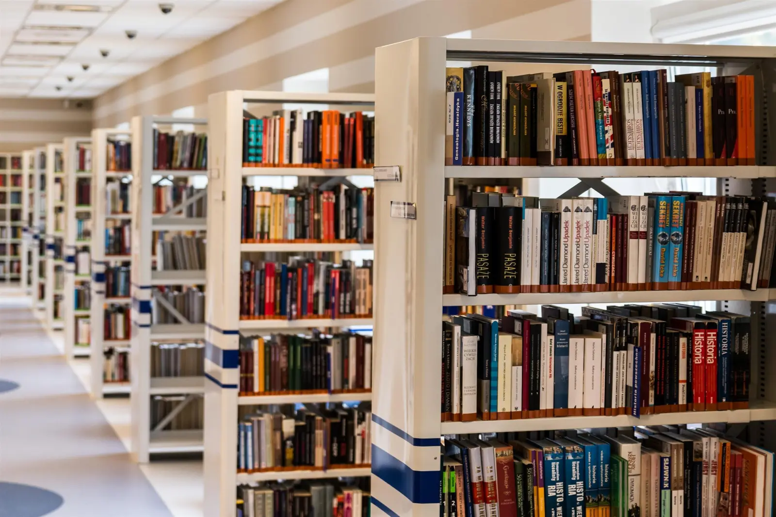 A perspective view of white library shelves filled with many books.
