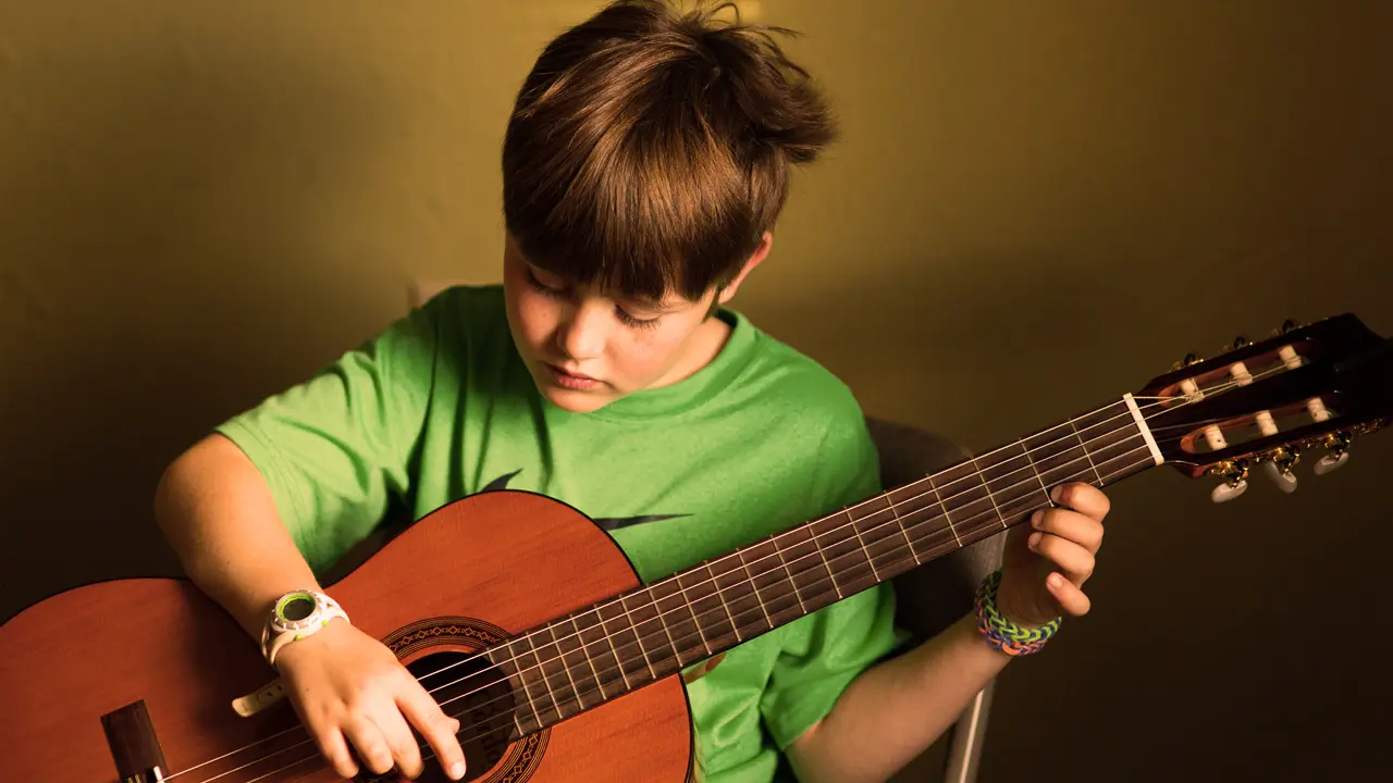 A young boy practices playing an acoustic guitar.
