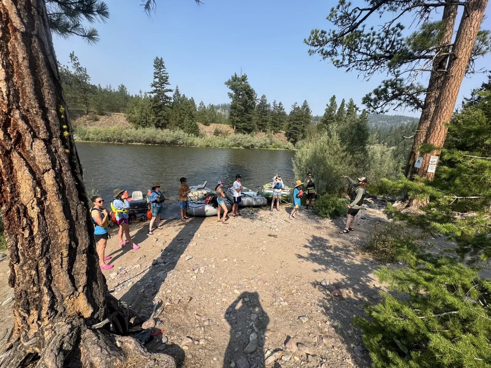 A group of people are gathered on a riverbank with rafts, with one individual appearing to provide instructions.