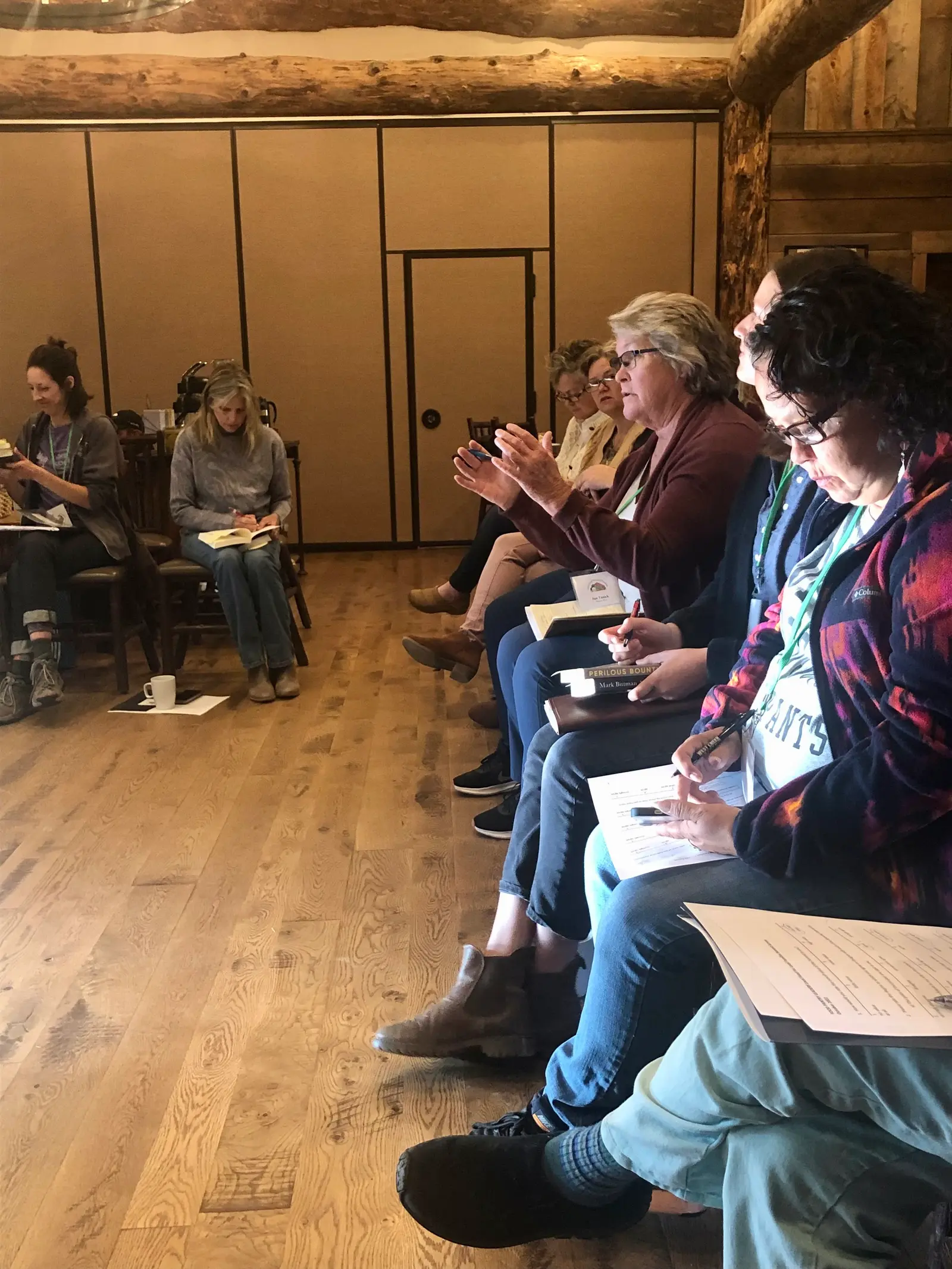A group of adults are seated in a rustic, wood-paneled room, attending a class or workshop.