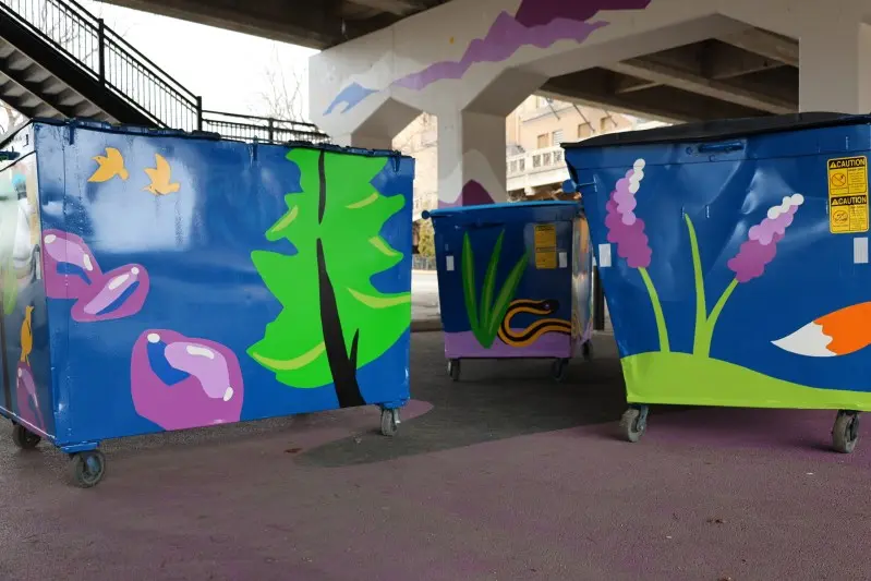 Three painted dumpsters sit underneath a concrete bridge.