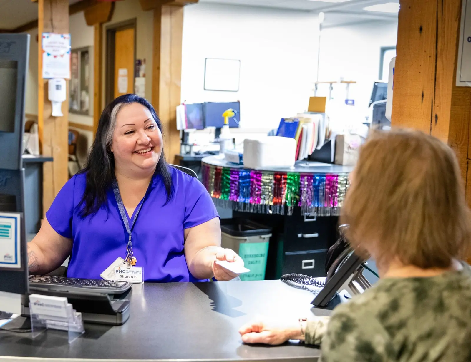 A woman smiles while handing a card to a person across a service desk.