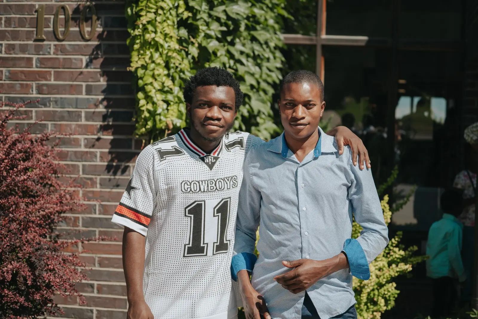 Two young men stand side-by-side with one's arm around the other's shoulder.