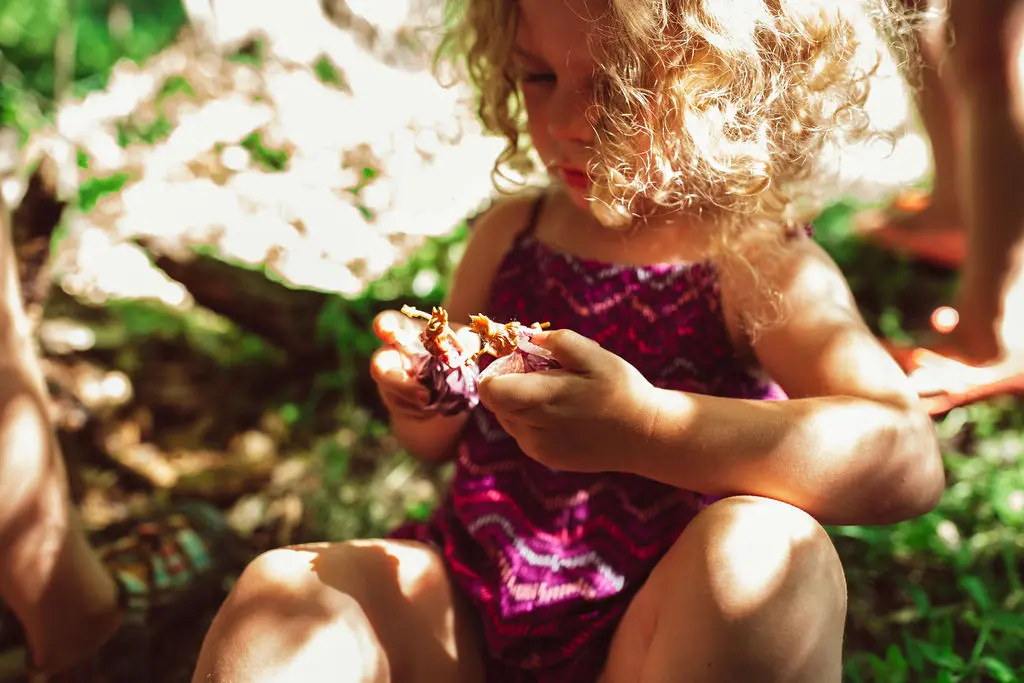 A young girl with curly hair sits outside while playing with small toy figures.