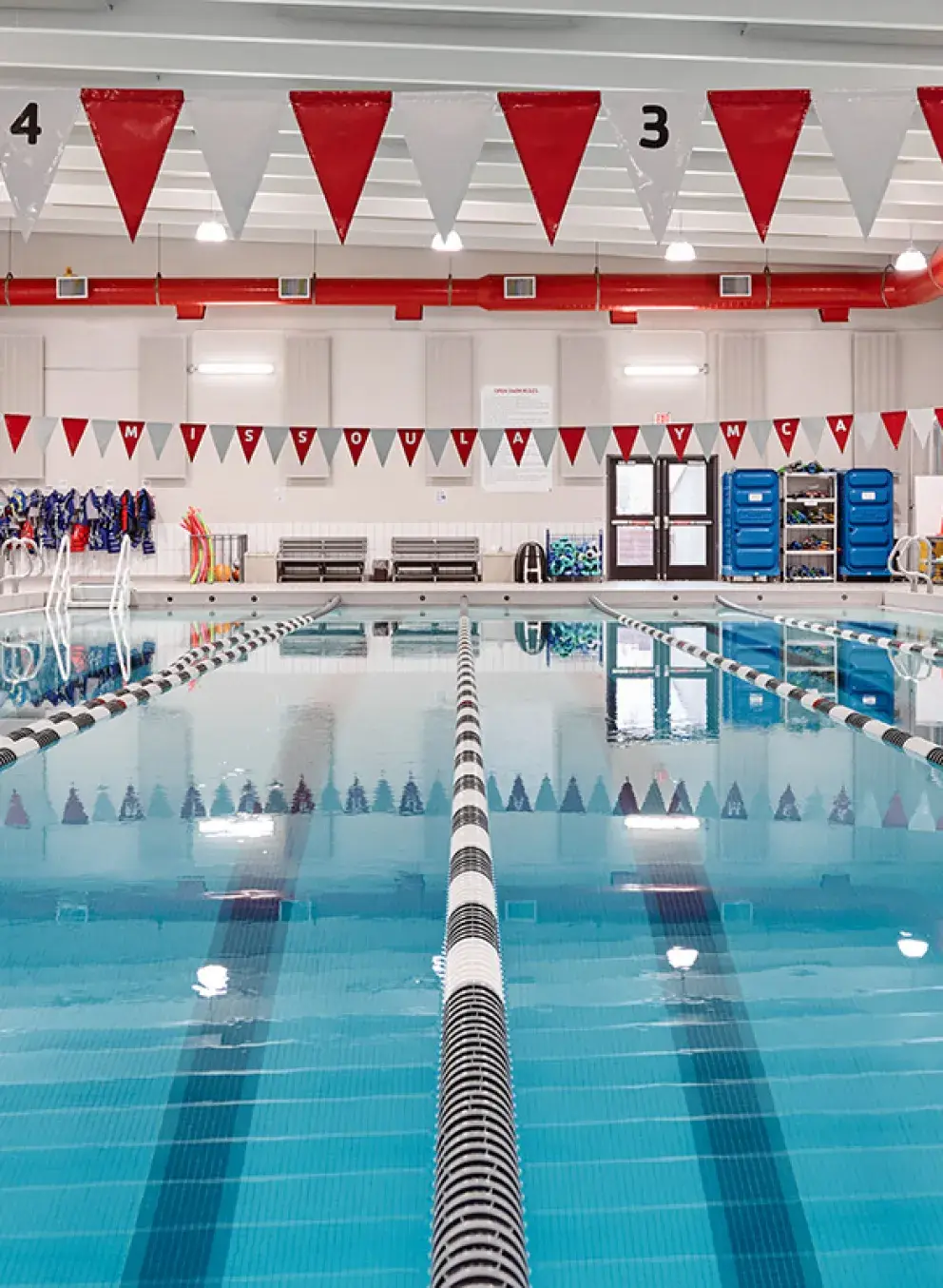 a photo of the missoula ymca's indoor 25-yard pool with black and white lap lanes. there is red and white flagging strung over the pool.