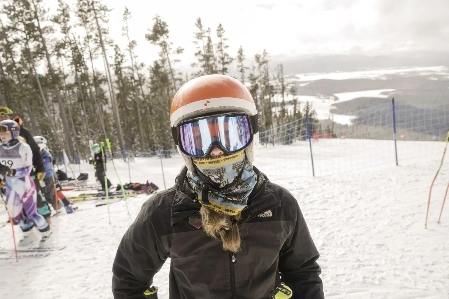 A skier wearing goggles and a helmet stands on a snowy slope with others in the background.