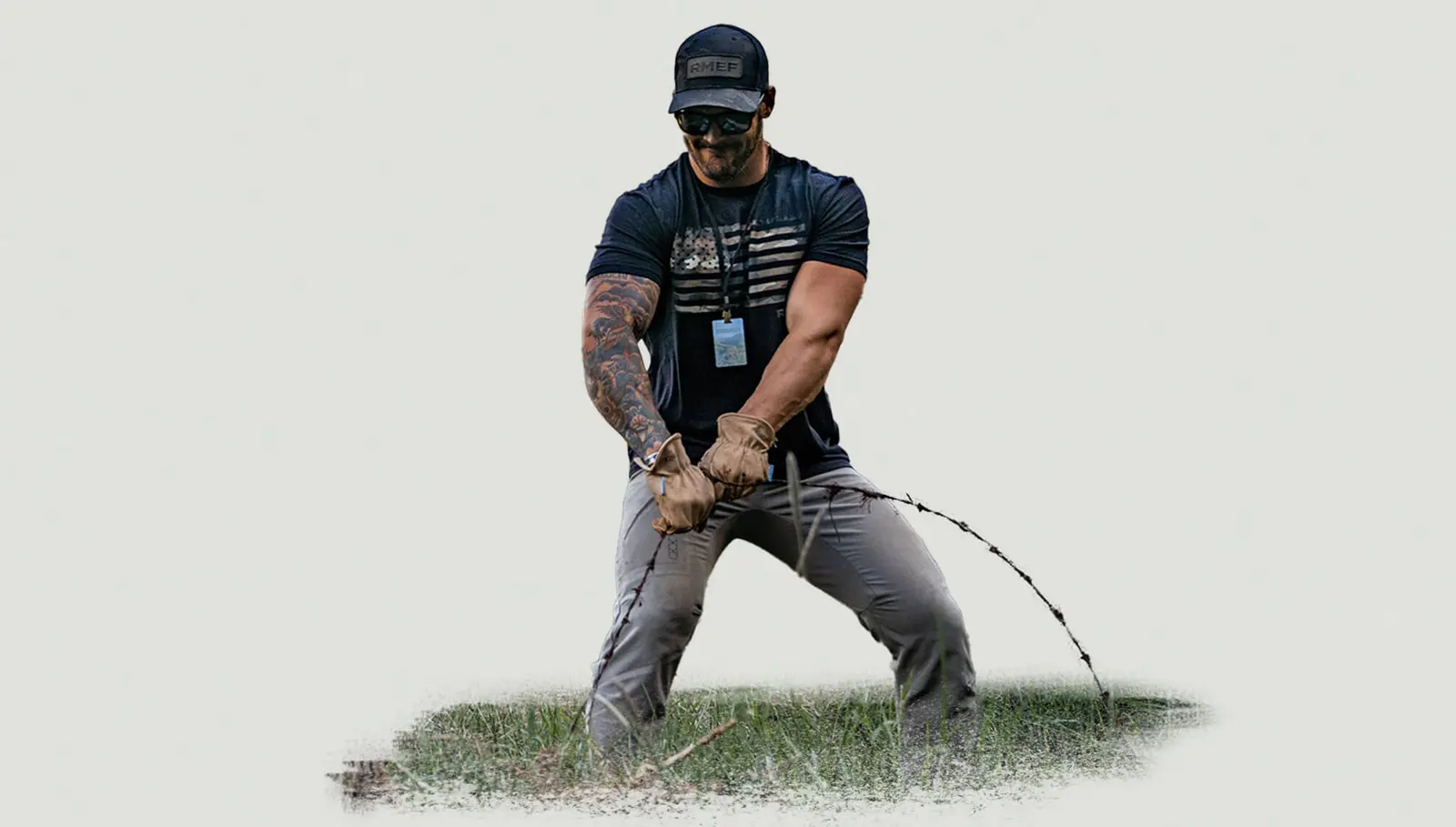 A man wearing gloves and a cap pulls on a wire in a grassy field.