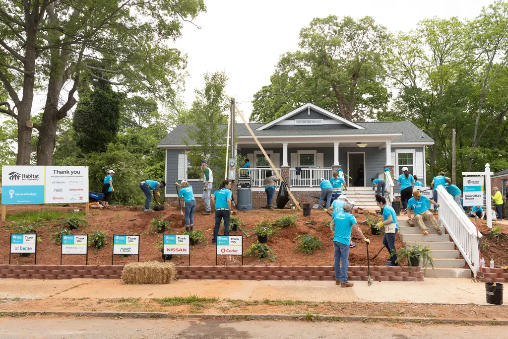 A group of volunteers in blue shirts works on landscaping in front of a house.