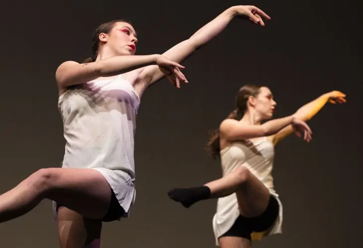 Two dancers in white gowns perform with their arms cast toward the right.