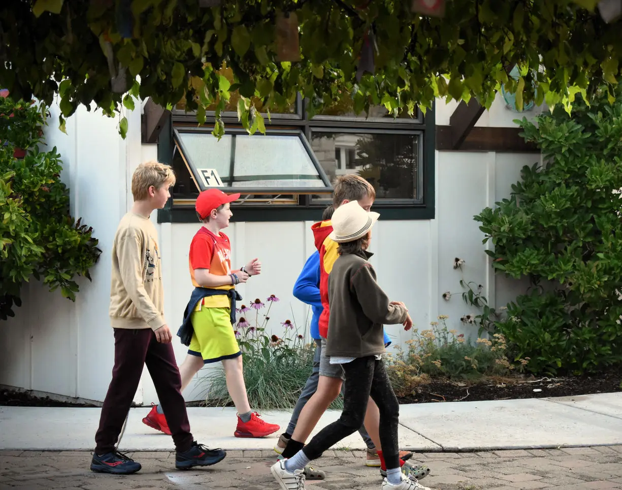 A group of children walks in a line on a sidewalk.