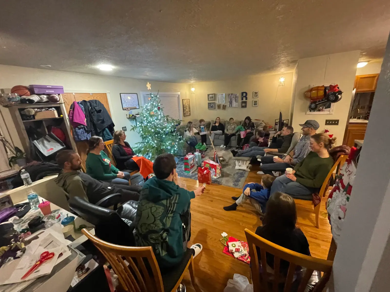 A group of people gather in a living room decorated for Christmas to exchange gifts.