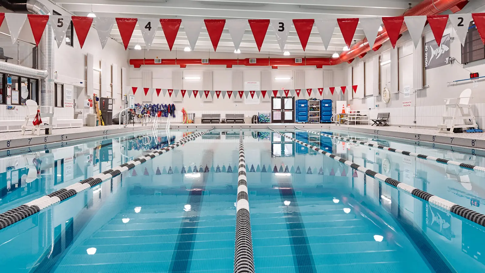 a photo of the missoula ymca's indoor 25-yard pool with black and white lap lanes. there is red and white flagging strung over the pool.