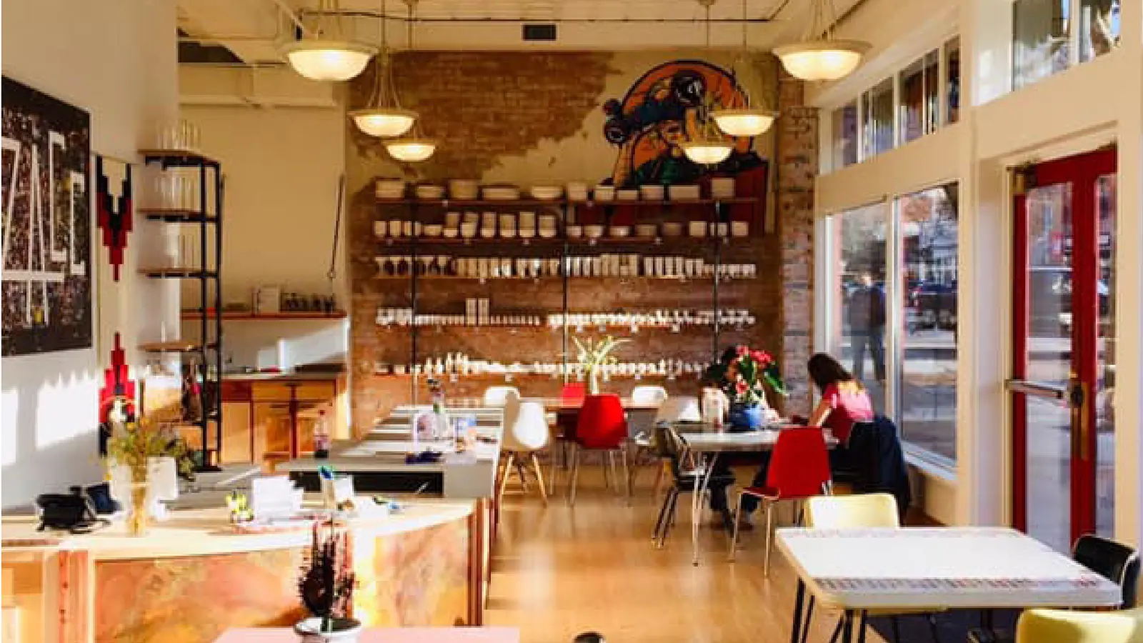 The interior of a brightly lit cafe with brick walls and dining tables.
