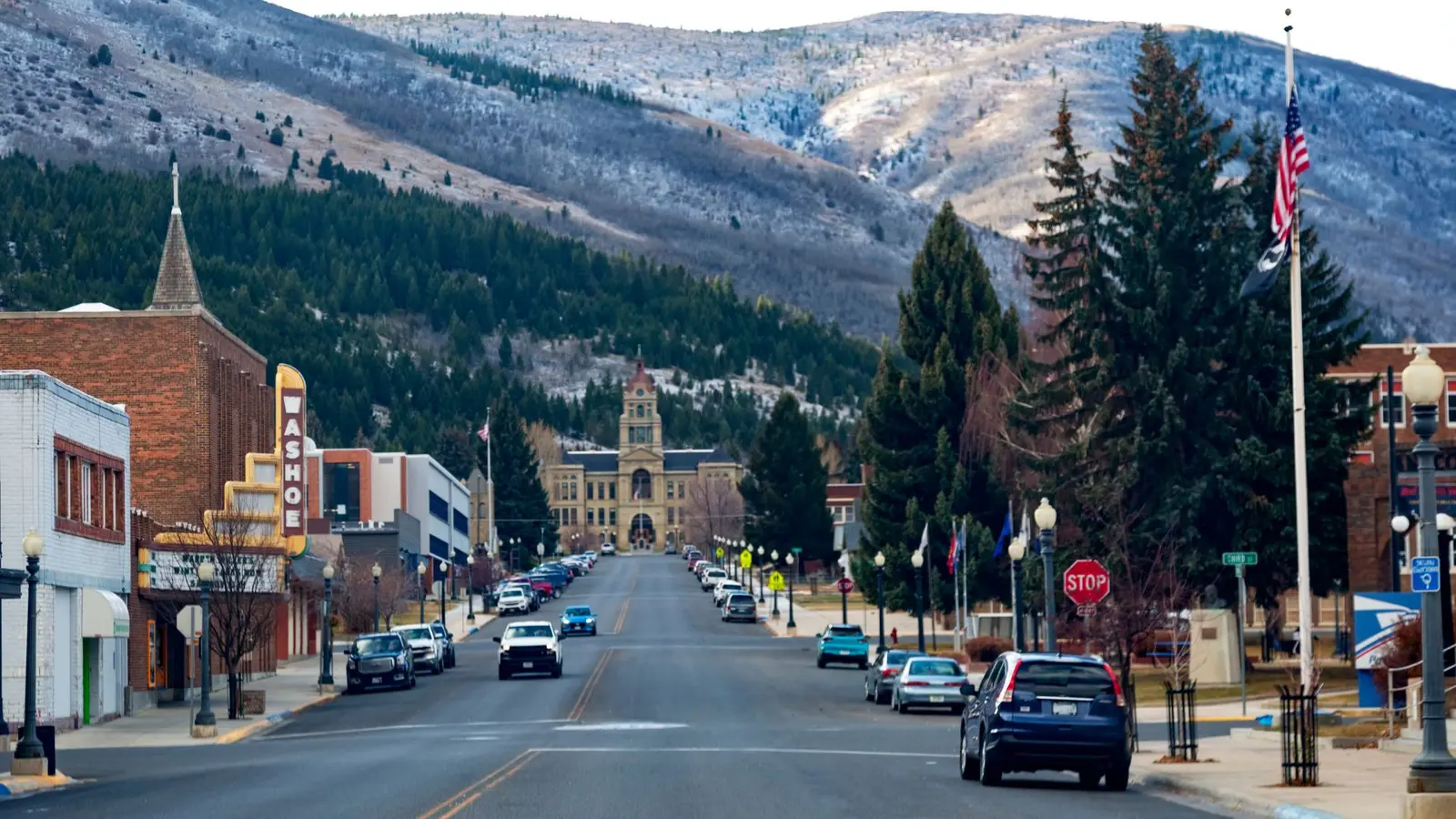 A street in a small town leads toward a large historic building at the base of a snowy mountain.