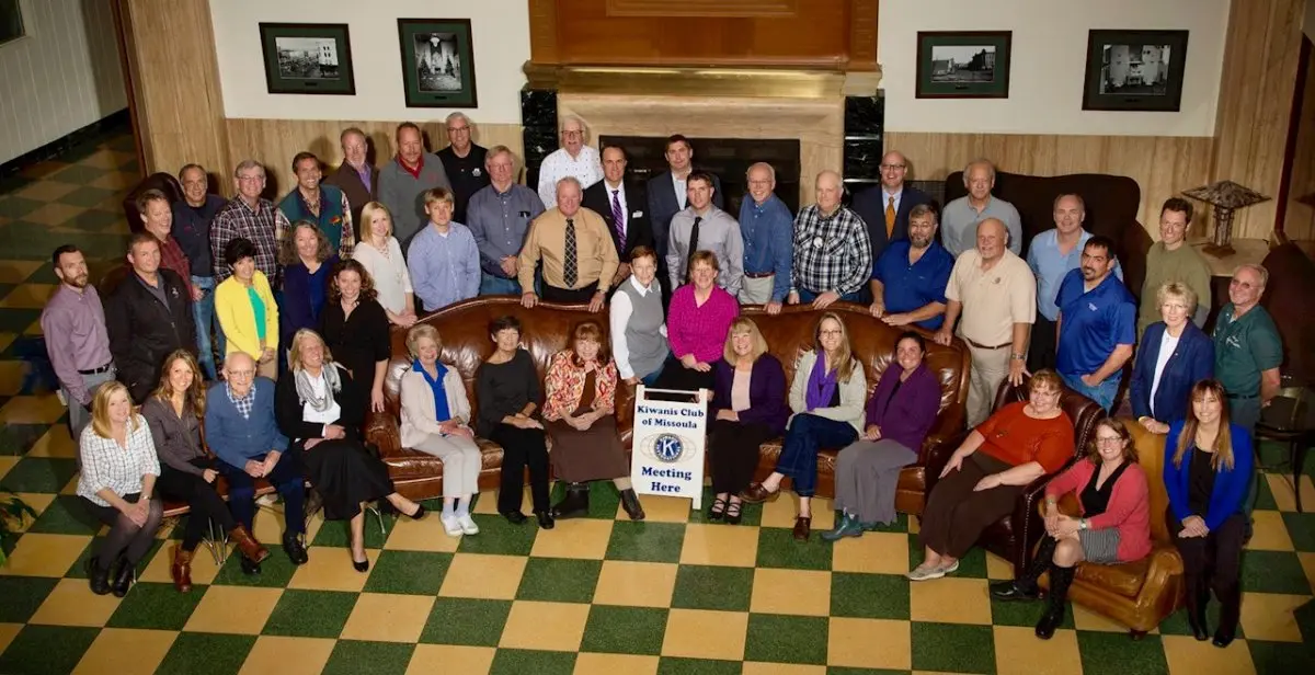 A large group of people poses for a photo in a room with a checkerboard floor and a prominent sign.